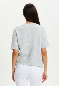 Light gray, short-sleeve knit sweater with a soft, fluffy texture, round neckline, and ribbed hem. Worn over white pants.