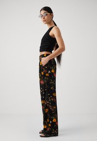 Svart cropped topp med teksturert stoff, kombinert med høy midje blomstrede bukser i livlige farger, med løs passform og lommer.