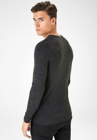 Suéter de punto gris oscuro con mangas largas, cuello redondo y dobladillo acanalado. Textura suave, diseño ajustado y un patrón jaspeado sutil.