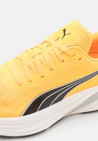 Scarpa da corsa gialla leggera con tomaia in mesh traspirante, lacci piatti e accenti laterali in bianco e nero. Suola imbottita per il comfort.