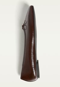 Chaussure plate en faux cuir marron avec un bout rond et un lacet décoratif. La texture lisse contraste avec la semelle mate. Vue latérale.