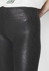 Svarta leggings med ormskinnsmönster som har en slät, glänsande yta och en åtsittande design, som visar subtila variationer i mönstrets djup.