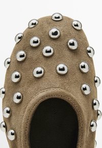 Scarpa slip-on in suede color tan, caratterizzata da borchie metalliche arrotondate disposte sulla tomaia, con un interno nero e senza lacci o chiusure visibili.