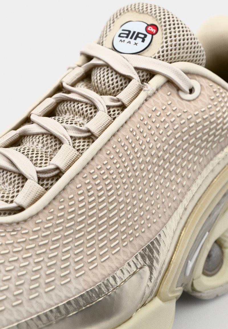 Helle beige Sneakers mit Obermaterial aus Netz und strukturiertem Leder, abgerundeter Form, sichtbaren Schnürsenkeln und einer markanten Luftpolstersohle.