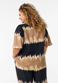 Kortärmad blus i svart och beige med ett texturerat, abstrakt randmönster. Lätt lös passform och mjukt, lättviktsmaterial.
