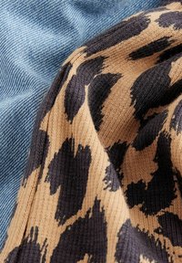 Tissu en tricot couleur beige avec des taches de léopard noires drape un denim bleu doux, mettant en valeur des textures et des motifs contrastants.