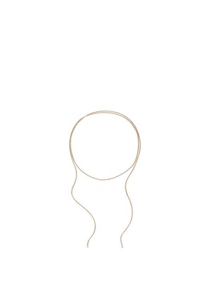 Collier fin en cordon beige avec de petites extrémités argentées ou métalliques, enroulé lâchement sur un fond blanc.