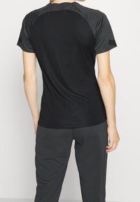 Svart träningsskjorta med kontrasterande texturerade grå korta ärmar, rund halsringning och slätt tyg. Bärs med gråa träningsbyxor.