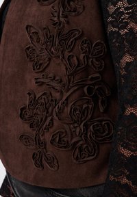 Donkerbruin suede stof met verhoogde bloemenapplicaties, gecombineerd met een zwarte kanten kledingstuk eronder.