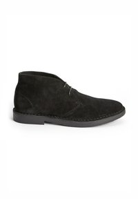 Black suede ankle boots with a smooth texture, featuring a rounded toe, minimalistic design, and two eyelets for laces.