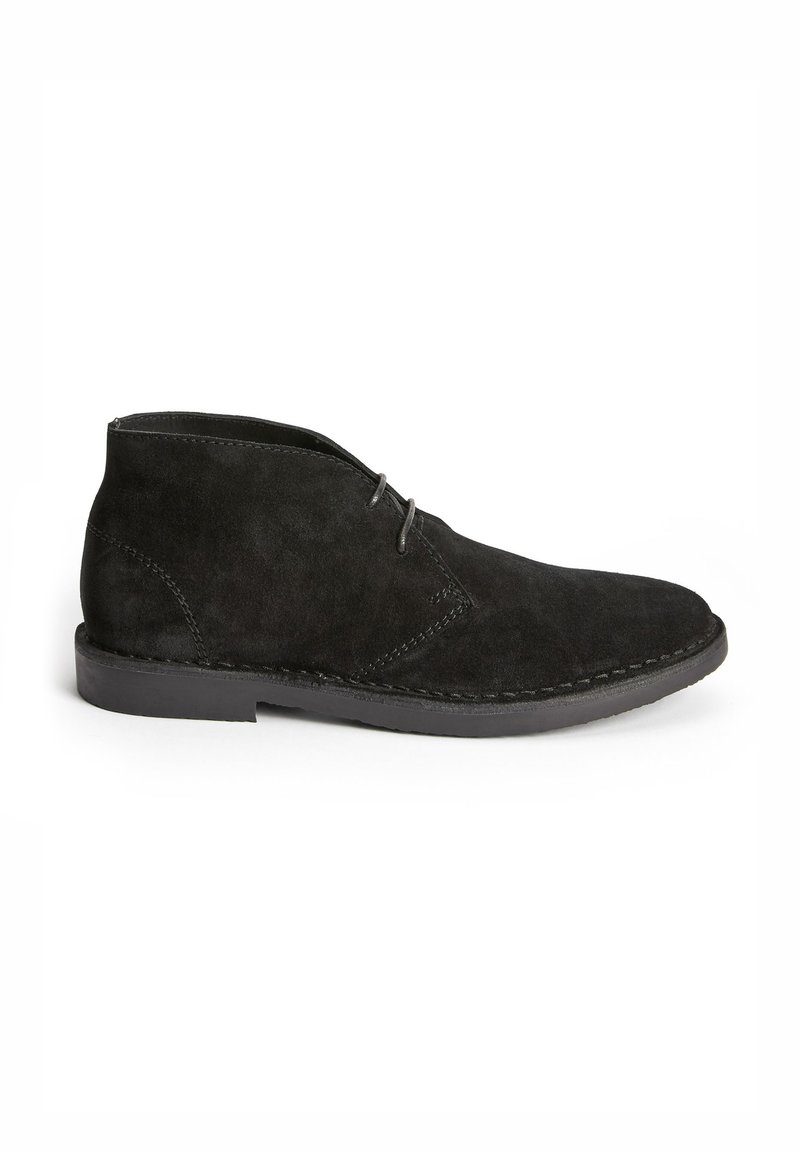 Black suede ankle boots with a smooth texture, featuring a rounded toe, minimalistic design, and two eyelets for laces.