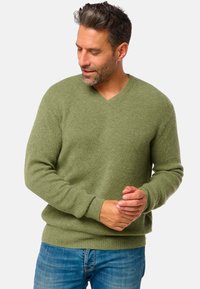 Pull vert côtelé en V fabriqué dans un matériau doux, avec des manches longues et une coupe décontractée, associé à un jean bleu.