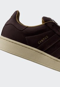 Low-top dark brown sneaker with beige sole, gold interior lining, and "CAMPUS" text embossed in gold on the side.