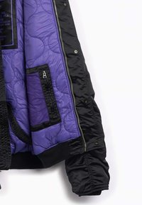 Giubbotto bomber nero con una fodera imbottita viola, dotato di chiusura con zip, tasche sulla fodera interna e polsini a costine.