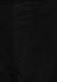Gros plan sur un tissu noir avec une couture verticale et un petit détail cousu près du coin inférieur gauche.