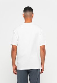 White cotton t-shirt with short sleeves, a crew neck, and a subtle tag detail on the back. Flat texture and casual fit.