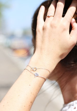 Zilveren armband met een delicate ketting, onderling verbonden ringen en een gestileerde boomhanger. De hand heeft een lichte huid en is gedeeltelijk bedekt door haar.