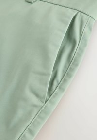 Gros plan sur la poche d'un pantalon vert clair avec des coutures visibles et la texture du tissu.