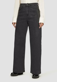 Jean large noir en denim, avec une texture lisse et orné de petits clous sur les poches avant.
