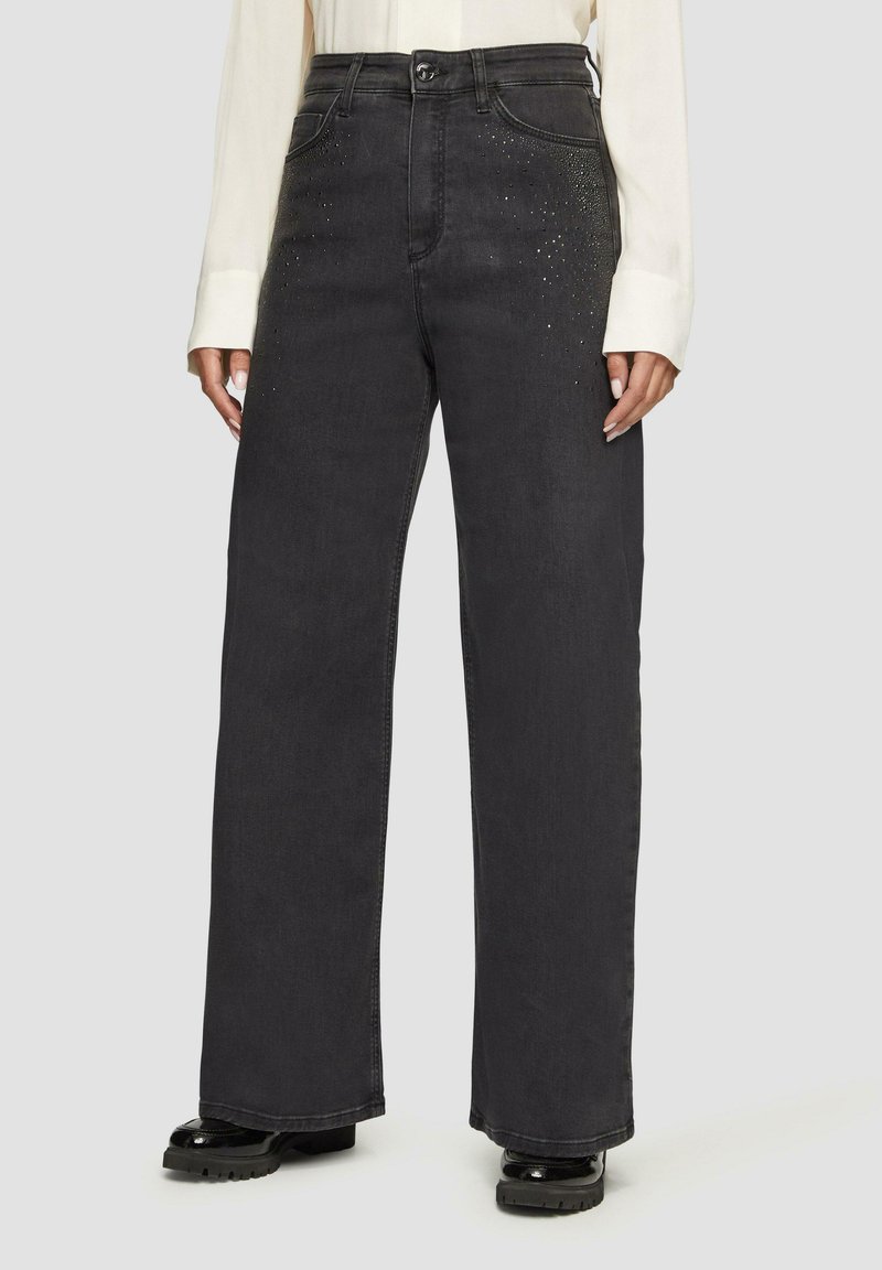 Jean large noir en denim, avec une texture lisse et orné de petits clous sur les poches avant.