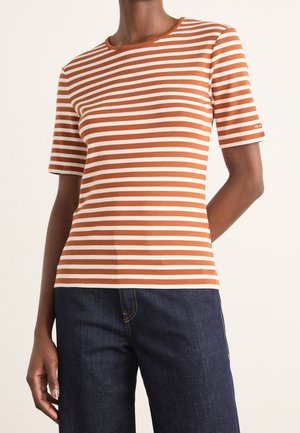 Person wearing a brown and white horizontal striped short-sleeve shirt paired with dark blue denim pants, against a plain background.