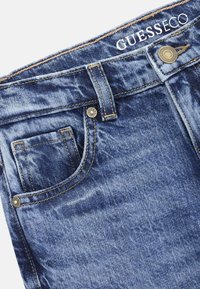 Jeans de mezclilla en azul oscuro con un acabado desgastado. Presentan un bolsillo frontal, botón metálico y detalles de costura. Etiqueta de la marca visible.