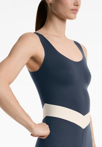 Navy blue swimsuit with a scooped neckline, wide shoulder straps, and contrasting cream chevron detail at the waist. Smooth texture.