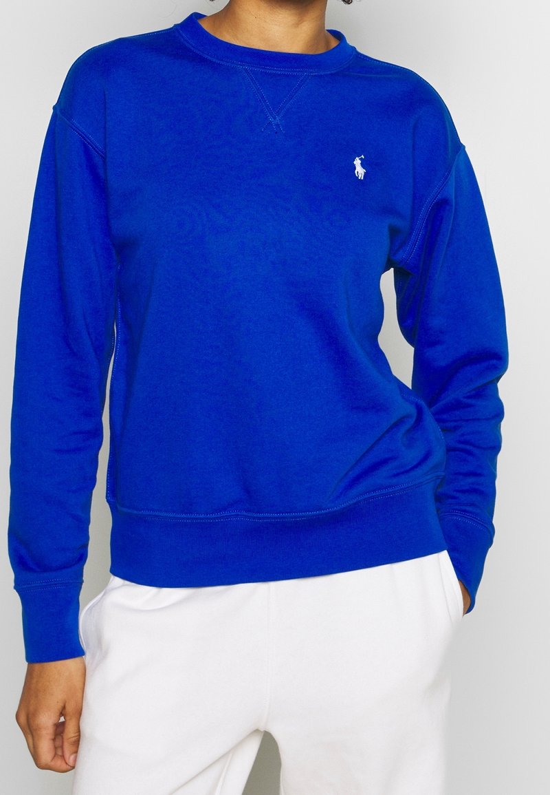 Blå bomulls sweatshirt med rundhals, ribbade ärmslut och nederdel, med en liten vit broderad logotyp på bröstet.