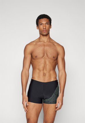 Bañador negro con un diseño ajustado, que presenta un patrón de líneas onduladas verdes en un lado. La tela es suave, lo que proporciona una apariencia elegante.