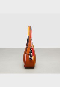 Kuvastoja sivulta monivärisestä nahkalaukusta, jossa on oranssi pohja, päällystetty paneelit ja kiinnitetyt kilpikonnakuosiset ja nahkamerkit.