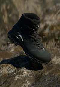 Czarna górska botka Scarpa zawieszona nad skalistym terenem, podkreślająca swoją wytrzymałą podeszwę i trwałą konstrukcję do użytku na zewnątrz.