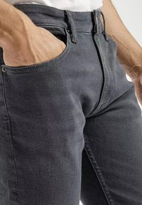Szare dżinsy o dopasowanym kroju, z klasycznym stanem i pięcioma kieszeniami. Teksturowana tkanina z subtelnymi detalami w szwach.