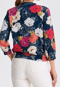 Blusa floral con fondo azul marino oscuro. Presenta flores coloridas en tonos de rosa, rojo y crema. Dobladillo fruncido y mangas con elástico.