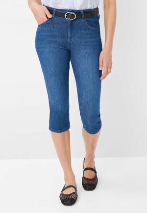 Pantaloni capri in denim blu scuro con una vestibilità aderente, orli risvoltati e tasche frontali; abbinati a ballerine in rete nere e una cintura nera.