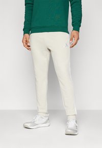 Bežiniai sportiniai keliai su šoninėmis juostomis, pagaminti iš minkštos medžiagos. Sujungti su baltais sportiniais bateliais, turinčiais tekstūruotą raštą ir raištelius.