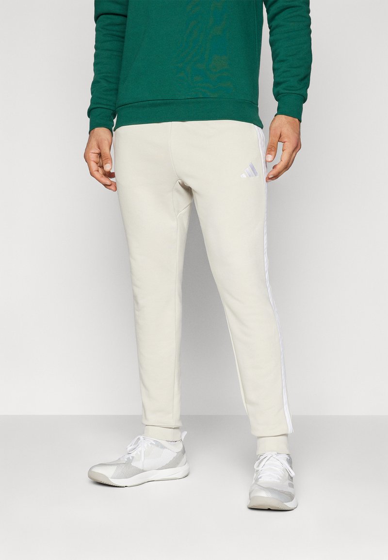 Bežiniai sportiniai keliai su šoninėmis juostomis, pagaminti iš minkštos medžiagos. Sujungti su baltais sportiniais bateliais, turinčiais tekstūruotą raštą ir raištelius.