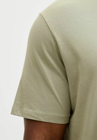 Camiseta de algodón verde oliva con una textura suave, manga corta y cuello redondo, que presenta un dobladillo limpio y un sutil detalle de costura.