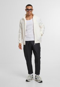 Valge tõmblukuga jakker kõrge kaelusega, sobitades valge tanki ja mustade pükstega. Tekstuuriga spordijalatsid täiendavad riietust.