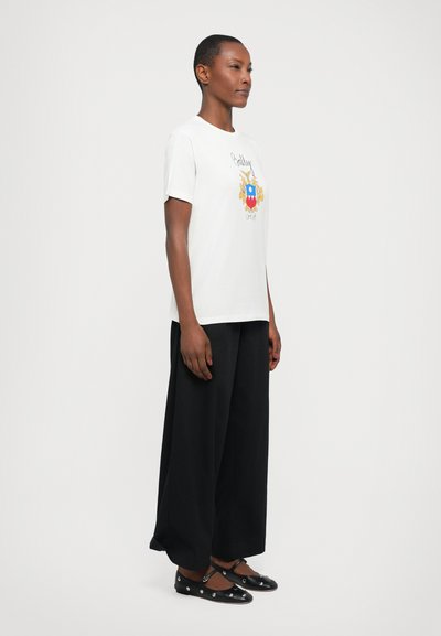 White short-sleeve t-shirt with a colorful graphic design, paired with black wide-leg trousers and black flat shoes featuring silver accents.