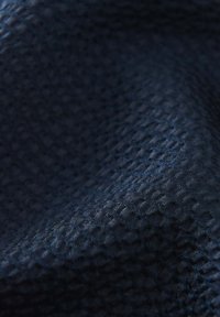Marineblauwe textuurstof met een geweven hexagonaal patroon. Het materiaal lijkt glad met een lichte glans en een zachte val.