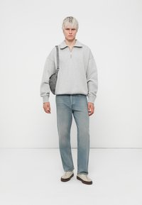 Vaaleanharmaa fleece-huppari, jossa on puoliveto, yhdistettynä vaaleansinisiin suoriin farkkuihin ja beigeihin lenkkareihin. Aksenina: pieni harmaa olkalaukku.