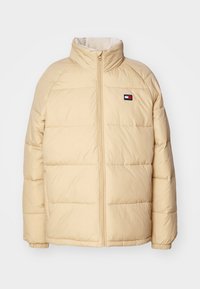 Beige puffer jacket with a high collar, zip front, quilted design, and elastic cuffs. Features a small logo emblem on the left chest.
