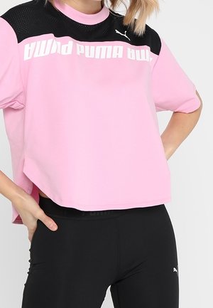 Osoba ubrana w luźną różowo-czarną koszulkę Puma z białym logo i dopasowane czarne legginsy Puma, stojąca z rękami na biodrach.