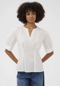 Bluză albă cu decolteu în V, mâneci bufante și talie ajustată. Fabricată dintr-un material neted, cu pliseuri în față și mansete ale mânecilor rulate.