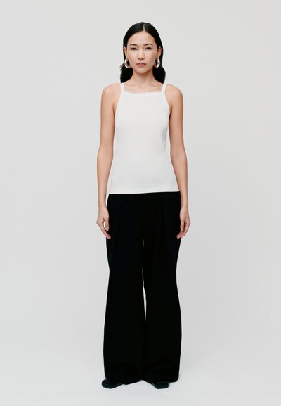 Top alb fără mâneci cu decolteu pătrat, asociat cu pantaloni negri, largi, cu talie înaltă. Material fin, design minimalist, fără modele.