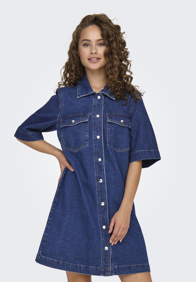 Denim shirt dress in dark blue, short sleeves, button front, two chest pockets, and light stitching details. Smooth texture, knee-length cut.