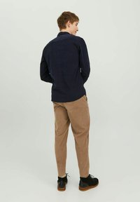 Camisa de manga larga azul marino con una textura suave, combinada con pantalones tapered color marrón claro y zapatos negros con suela marrón.