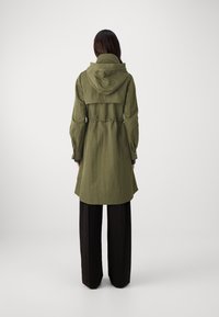 Cappotto trench verde oliva con cappuccio, vita cinchata e maniche lunghe. Presenta una vestibilità rilassata e un tessuto leggermente strutturato.
