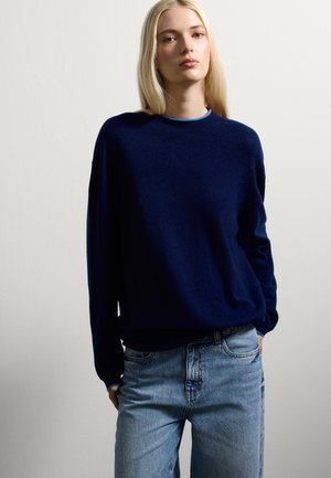 Pull en maille bleu marine avec un col rond et des manches longues, associé à un jean en denim bleu clair. Texture douce et coupe décontractée.