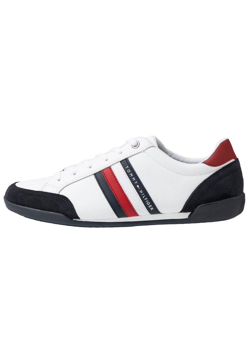 Vit låg sneakers med svarta och röda ränder, svart mocka tå och häl, samt en röd hälflik, märkt med Tommy Hilfiger-logotypen.